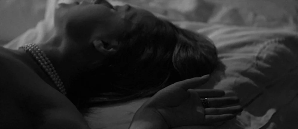 Les Amants (1958) movie still: closeup — A person rests on white bedding with their head turned to the side. The subject wears a pearl necklace and…