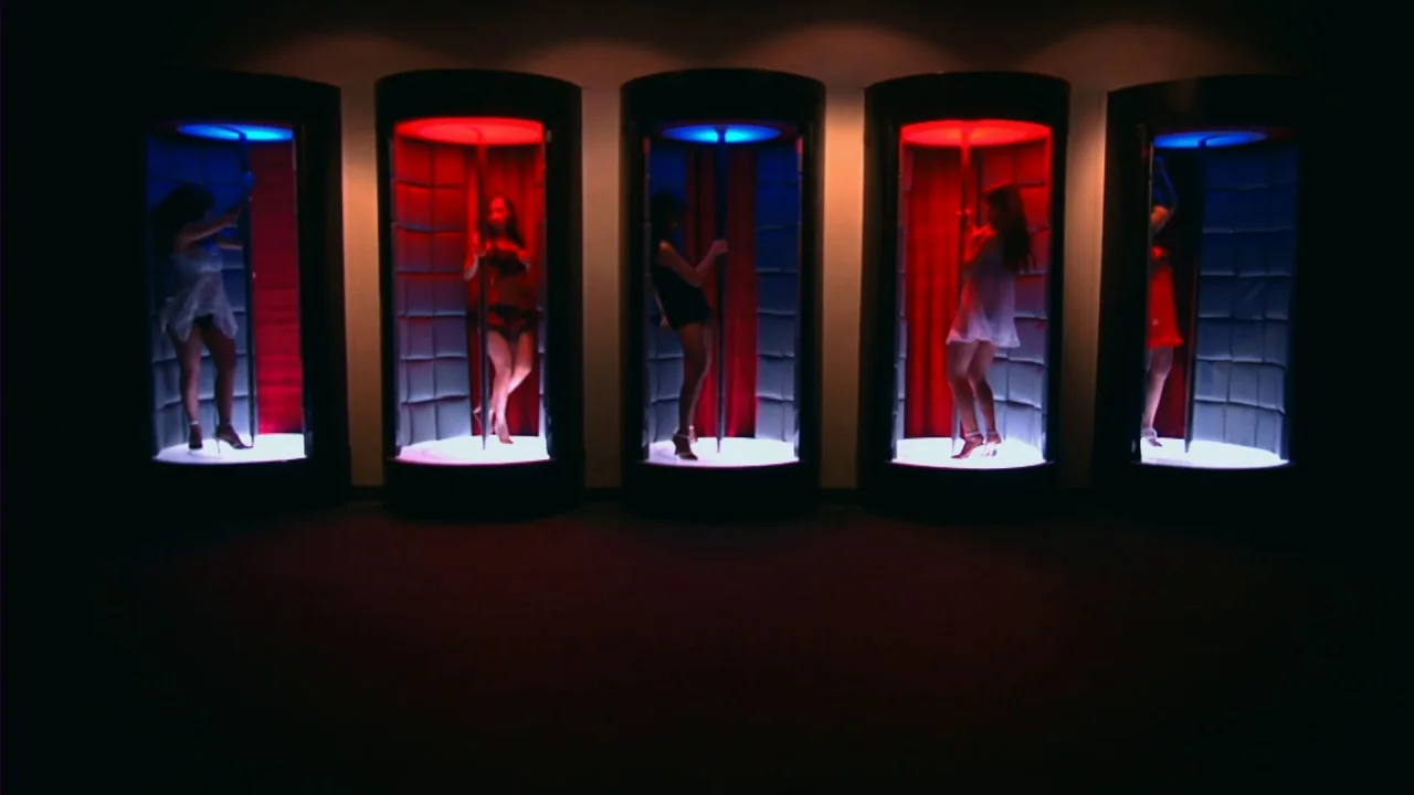 Merantau (2009) movie still: wide — Five cylindrical booths are lined up in a darkened room with red and blue lighting. Five women in short dresses…
