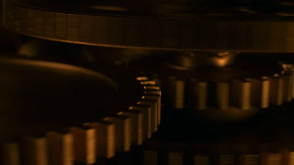 Cronos (1993) movie still: closeup — Intricate metal gears interlock within a dimly lit mechanical clock structure. The teeth of the gears catch…