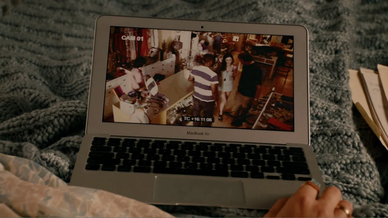 This Is 40 (2012) movie still: closeup — A close-up of a silver laptop resting on a thick, grey knitted blanket. The screen displays grainy…