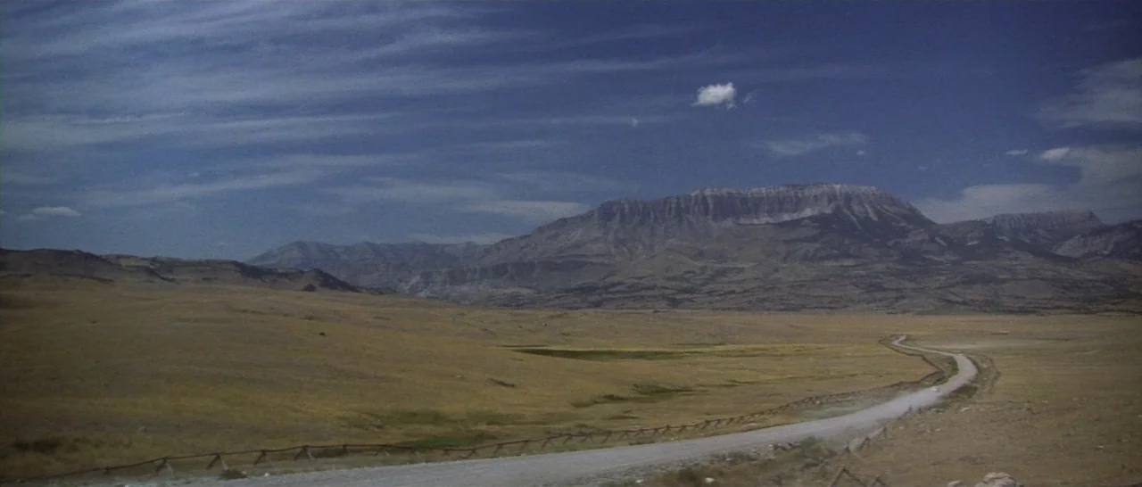 Thunderbolt & Lightfoot (1974) movie still: establishing — A wide expanse of rolling, dry grassy plains sits beneath a vast, cloudy blue sky. A…