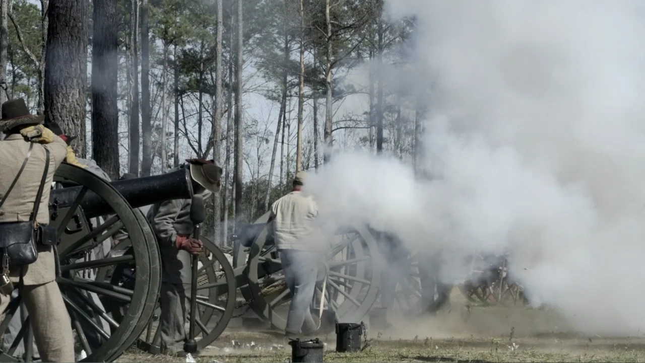 Kill Cavalry (2021) movie still: wide — A clearing in a dense pine forest contains multiple large artillery cannons. Men in historical military…