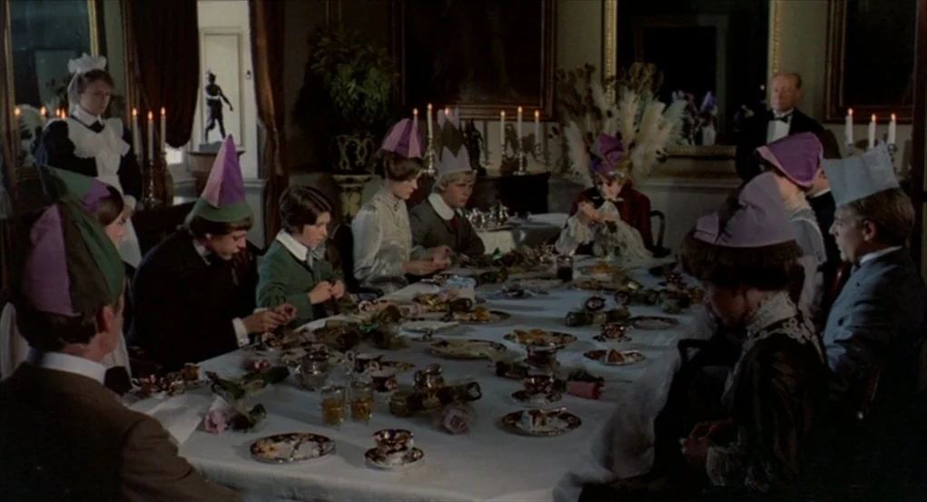 The Go-Between (1971) movie still: wide — A group gathers in an ornate dining room for a festive meal. The participants wear paper party hats while…