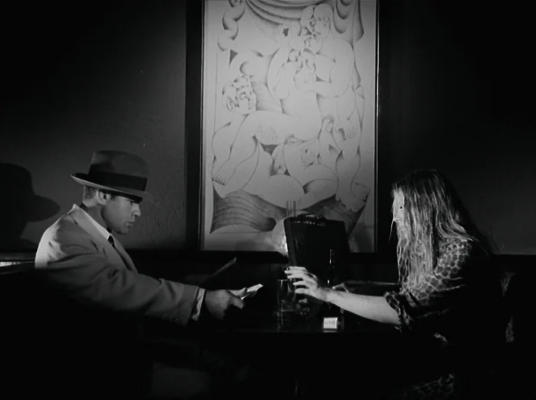 The American Soldier (1970) movie still: medium — A dark booth in a dim space featuring a large piece of surreal artwork. A man in a hat passes a…