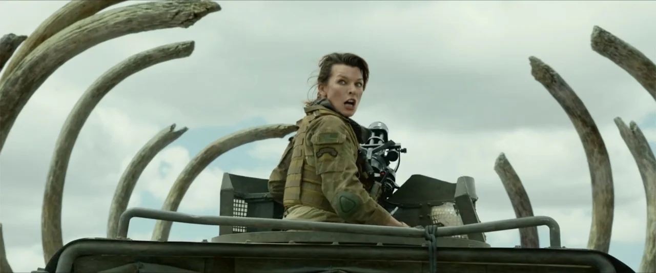 Monster Hunter (2020) movie still: medium — A soldier stands inside the hatch of a vehicle surrounded by giant curved bones. The woman glances…