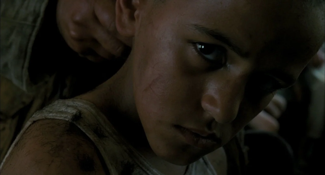 Incendies movie still: closeup — A dimly lit, cramped space with dark surroundings indicative of austere living conditions. A young boy stares ahead…