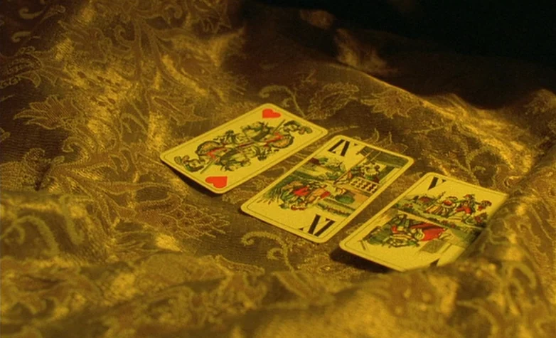 The Double Life of Véronique (1991) movie still: closeup — Three vintage European-style playing cards are positioned on a heavy, gold-colored…