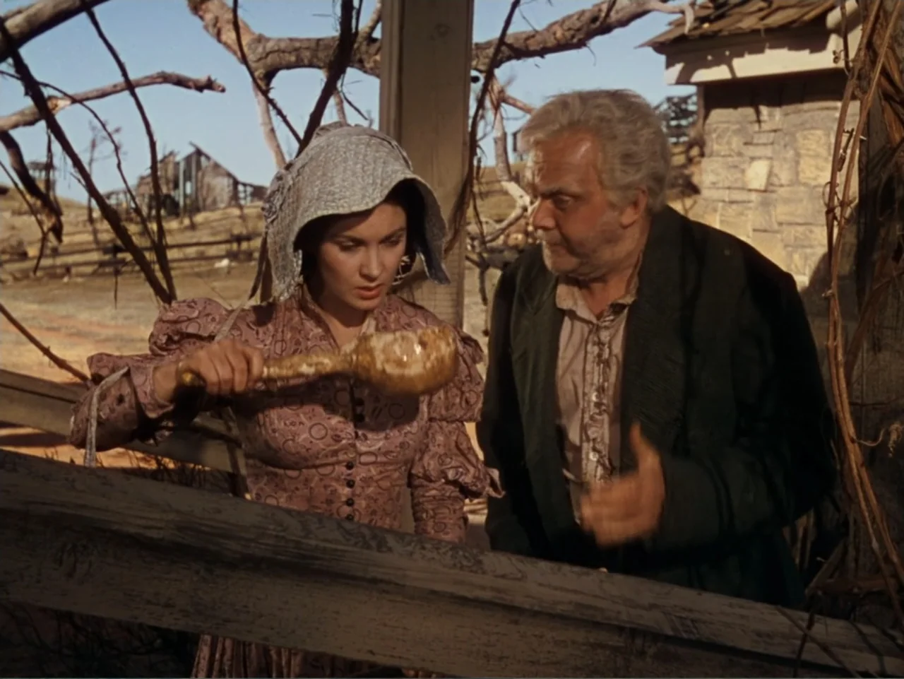 Gone with the Wind (1939) movie still: medium — An outdoor area with a wooden fence and a partially visible structure nearby. A young woman and an…