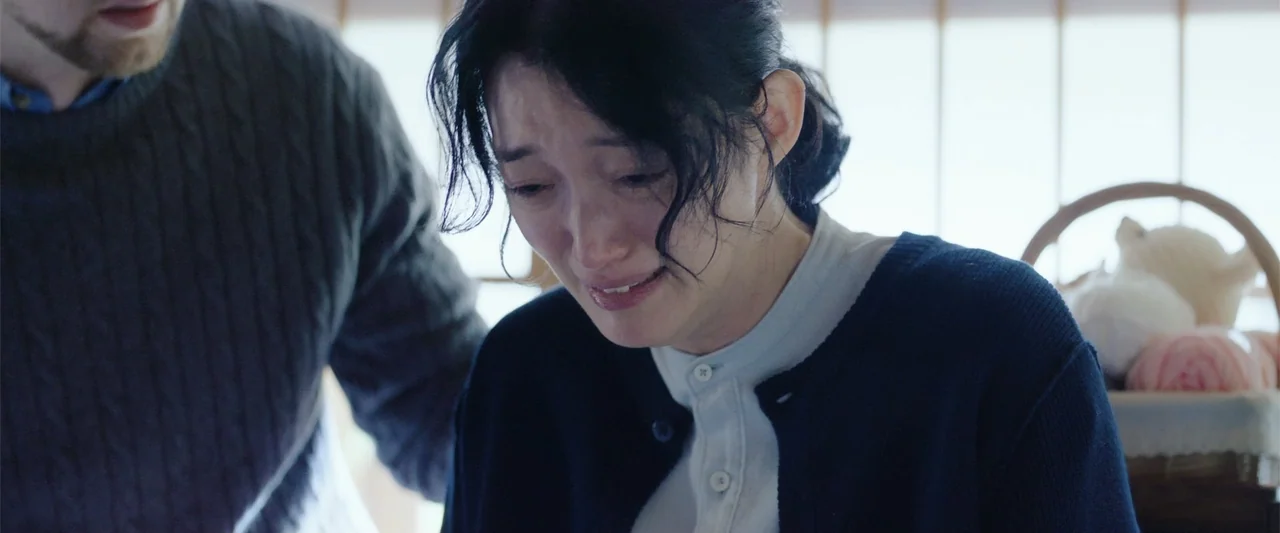 Angel Flight THE MOVIE (2026) movie still: medium — A light-filled room with a window and a basket of yarn in the background. A woman in a dark…