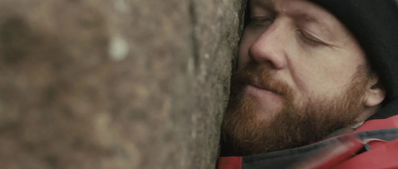 Sightseers (2012) movie still: closeup — A man's face presses against the coarse, weathered surface of a large natural rock. The rugged stone…
