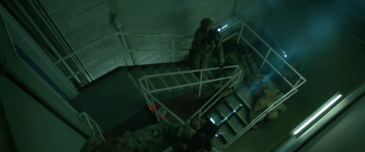The Predator (2018) movie still: wide — A utilitarian industrial stairwell features concrete block walls and white painted metal railings. Multiple…