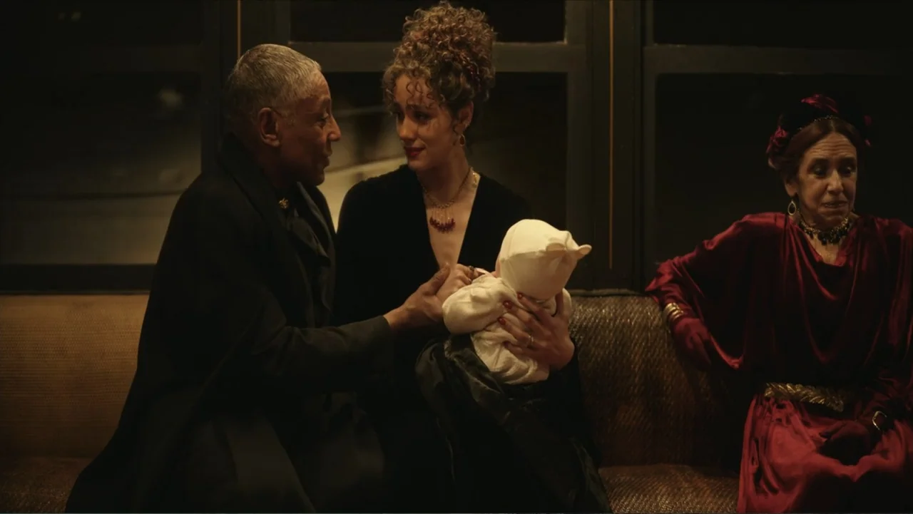 Megalopolis (2024) movie still: medium — An interior lounge features a dimly lit area with dark walls and a plush sofa. A man and a woman sit beside…