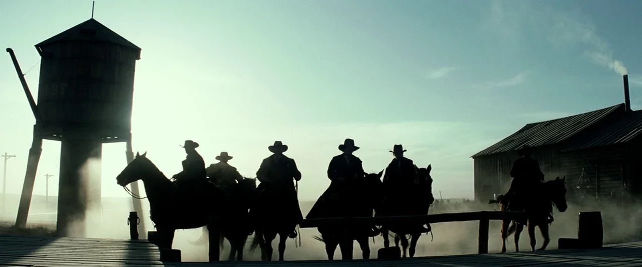 The Lone Ranger (2013) movie still: wide — A dusty 19th-century frontier train depot features a tall wooden water tower and barn. Several…