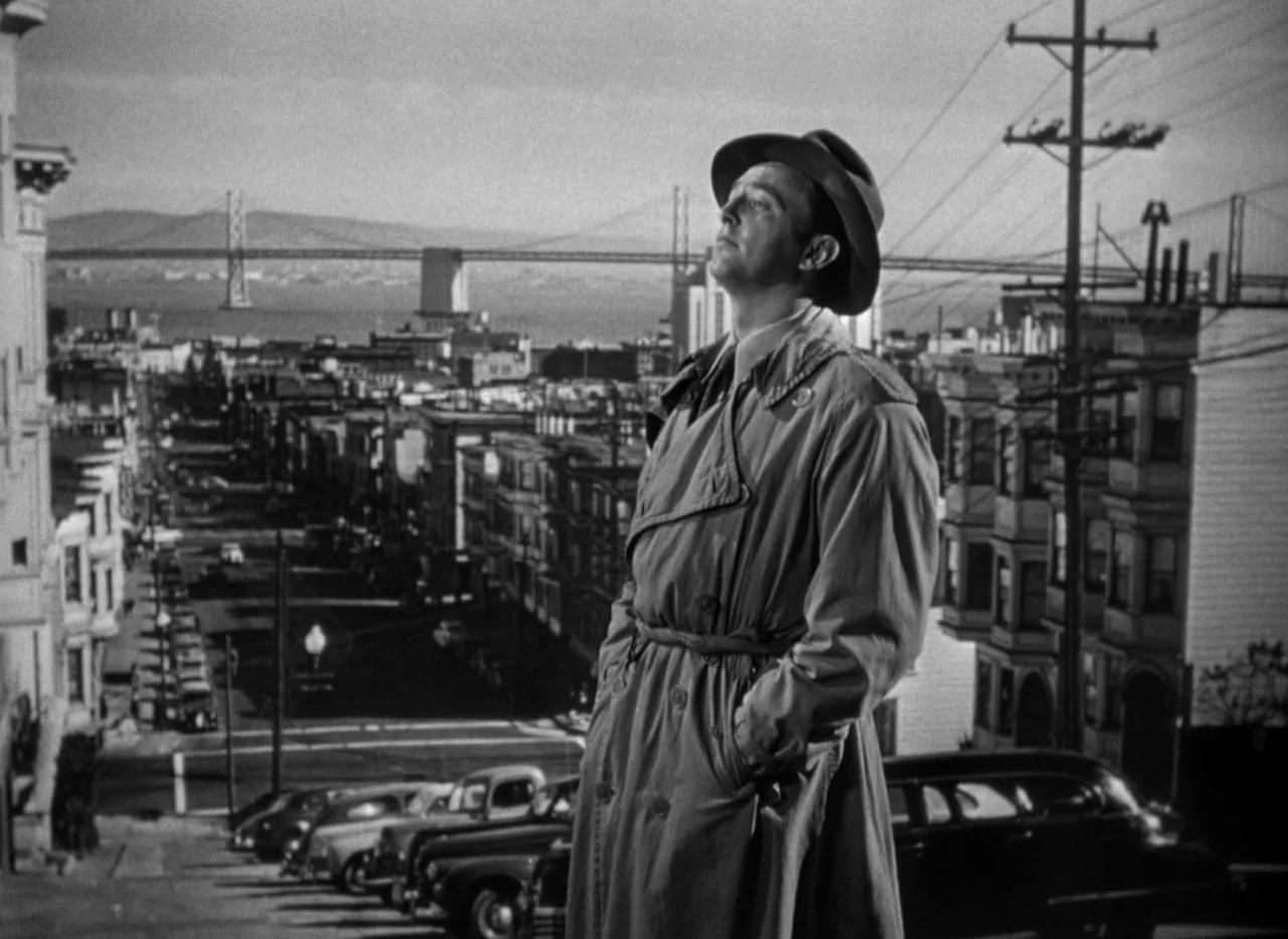 Out of the Past (1947) movie still: medium — A man stands on a San Francisco hill overlooking the bay and bridge. He faces away from the city street…
