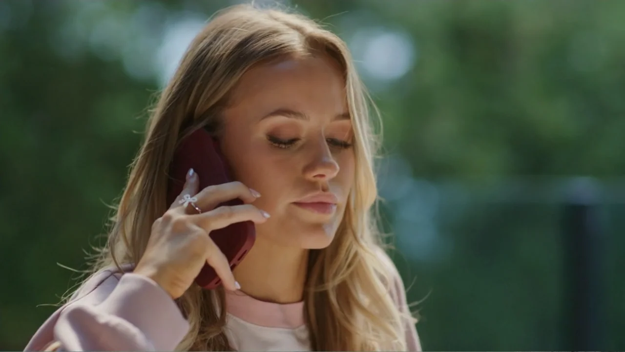 Christmas in the Spotlight (2024) movie still: closeup — A person stands outdoors against a background of blurred foliage and trees. A young woman…