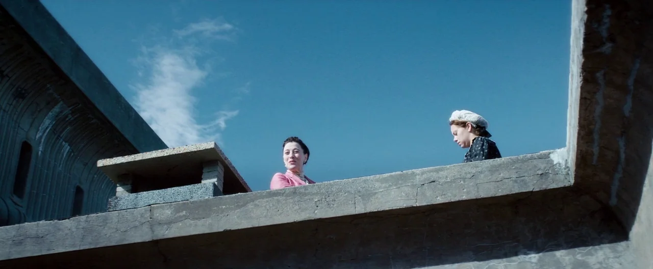 Slack Bay (2016) movie still: wide — Two women stand on a stark concrete structure against a clear blue sky. They look over the edge of the…