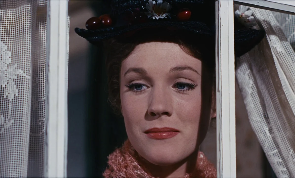Mary Poppins (1964) movie still: closeup — A woman stands behind a window frame with white curtains on either side. She looks outward with a neutral…