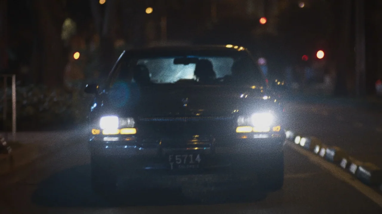 An Affair: A Dangerous Sexual Play (2014) movie still: medium — A dark sedan with illuminated headlights travels along a city street at night. The…