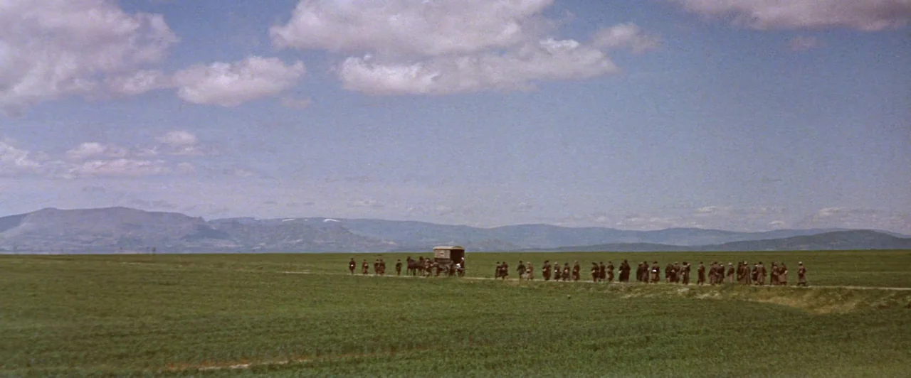 Doctor Zhivago (1965) movie still: wide — A vast, open green landscape stretches toward distant, layered mountains under a cloudy sky. A long line…