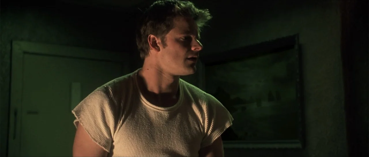 Joy Ride (2001) movie still: medium — A dimly lit interior room features textured walls and a framed painting on display. A young man in a white…