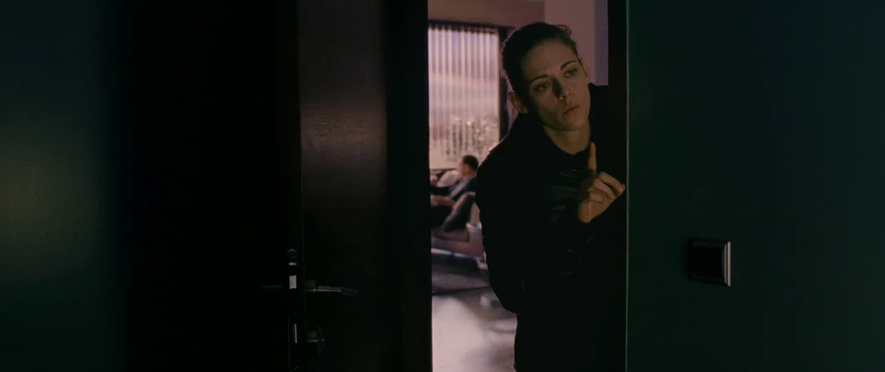 Personal Shopper (2016) movie still: medium — A dark hallway transitions into a bright room visible through a partially opened wooden door. A person…