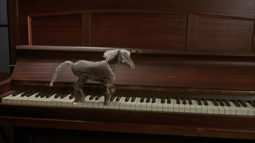 The Science Of Sleep (2006) movie still: medium — A dark polished wood piano sits in an interior room with keys exposed. A small fabric horse toy…