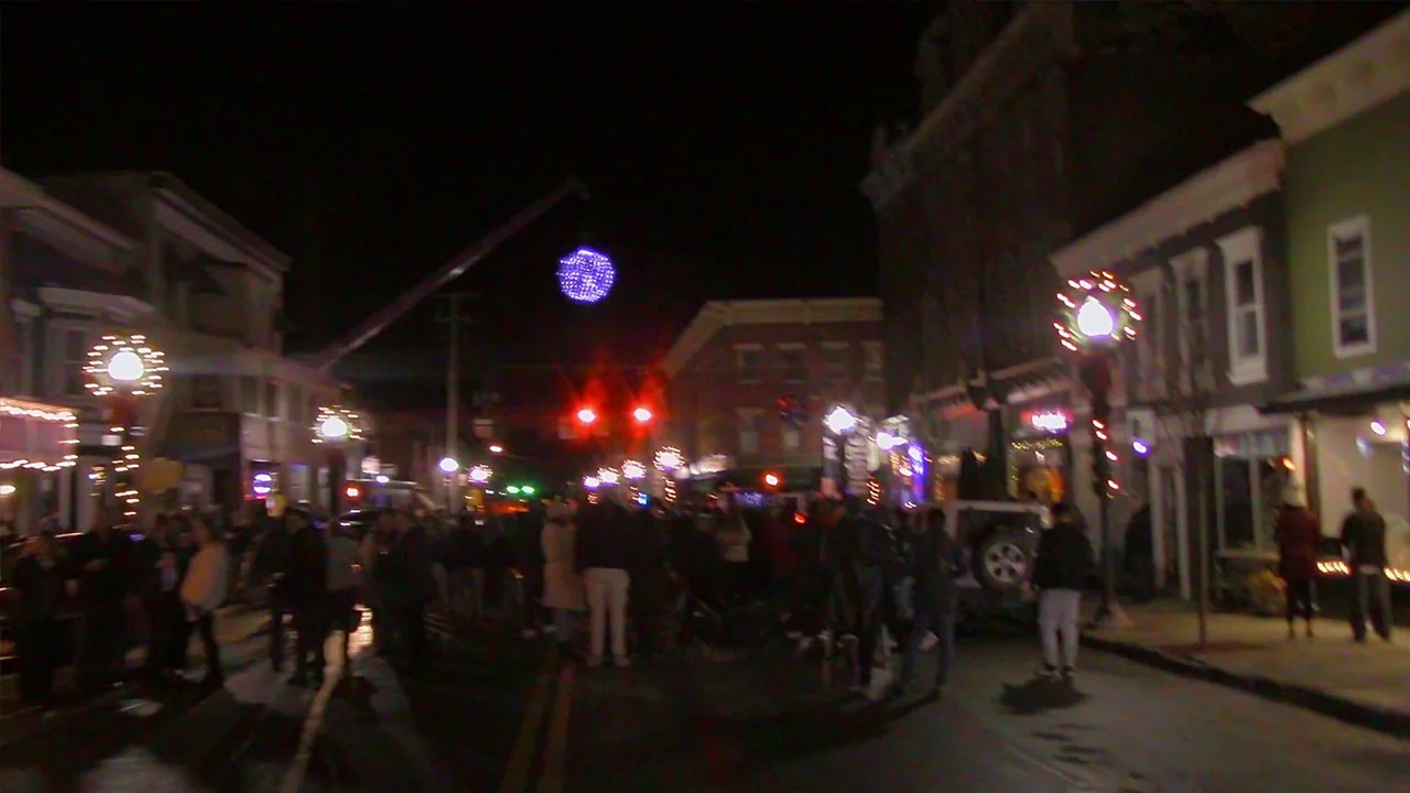 We’re All Going to the World’s Fair (2021) movie still: wide — A small town main street at night is filled with people during a public event. A…