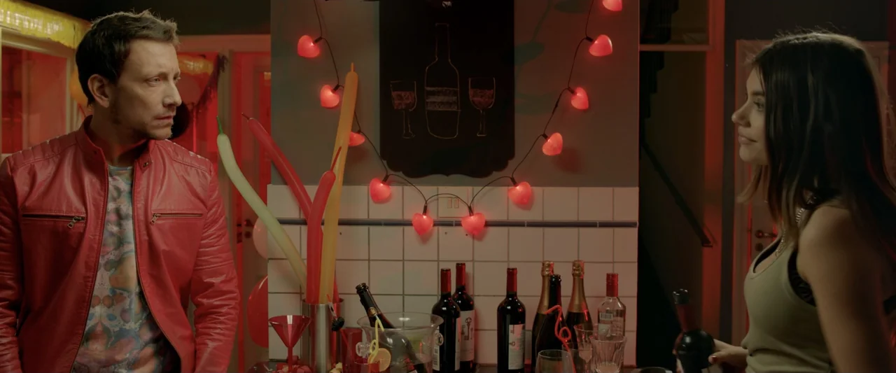 Perdida (2018) movie still: medium — A dimly lit bar counter is decorated with red heart-shaped string lights and bottles. A man and a woman stand…