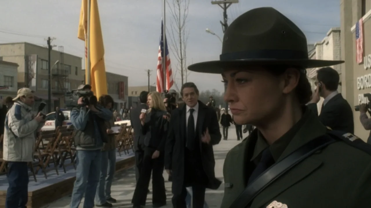 The Shepherd (2023) movie still: medium — An outdoor event is set on a sidewalk lined with folding wooden chairs. A woman in a military-style…