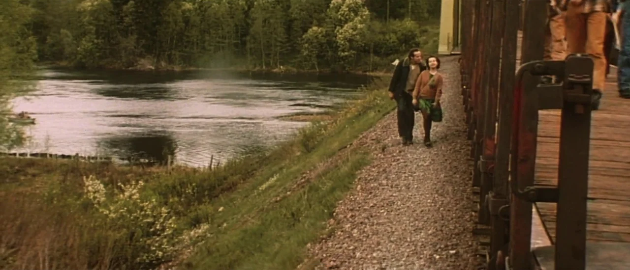 Dancer in the Dark (2000) movie still: wide — A rural landscape features a river running alongside a gravel railway embankment. A man and a woman…