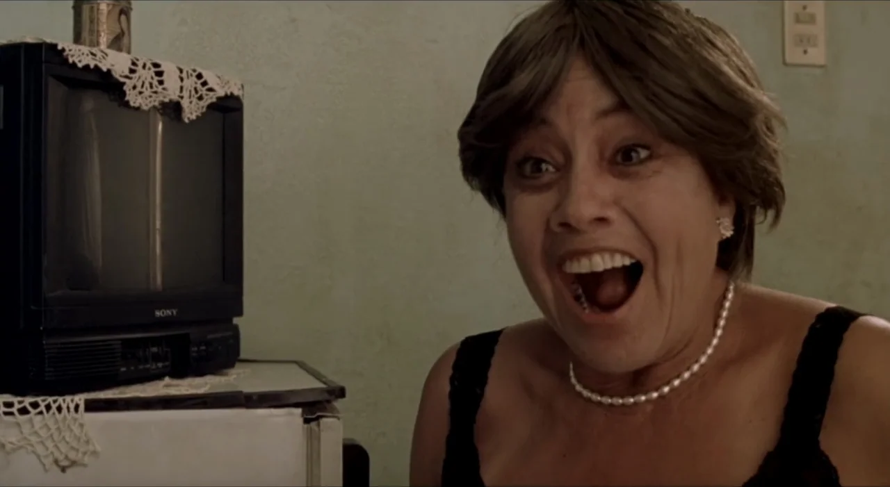 Sex, Love And Other Perversions II (2006) movie still: closeup — A woman's face is positioned in the foreground of a room with a TV set. The subject…