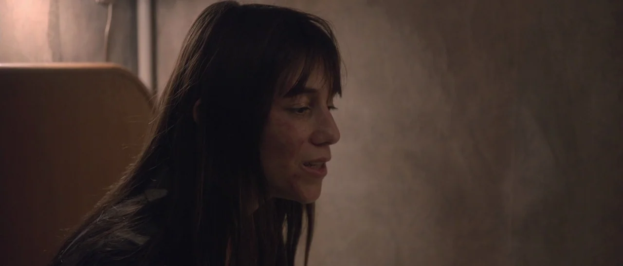 Nymphomaniac Vol 2 (2013) movie still: closeup — A dimly lit room with plain, textured walls and a subtle warm light source. A woman with long brown…
