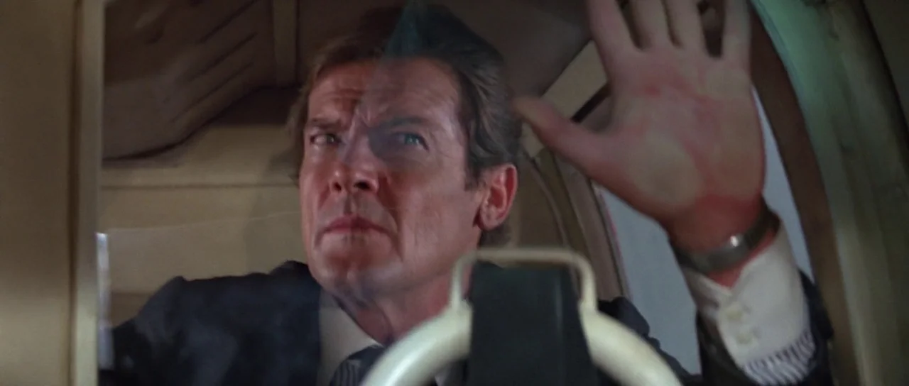 For Your Eyes Only (1981) movie still: closeup — A cramped cockpit with light tan interior panels and a metallic control yoke. A man in a dark suit…
