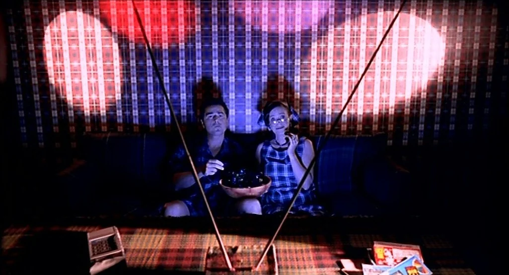 Nowhere (1997) movie still: medium — A 1950s living room features a plaid wallpaper backdrop and a vintage television set. A couple sits together on…