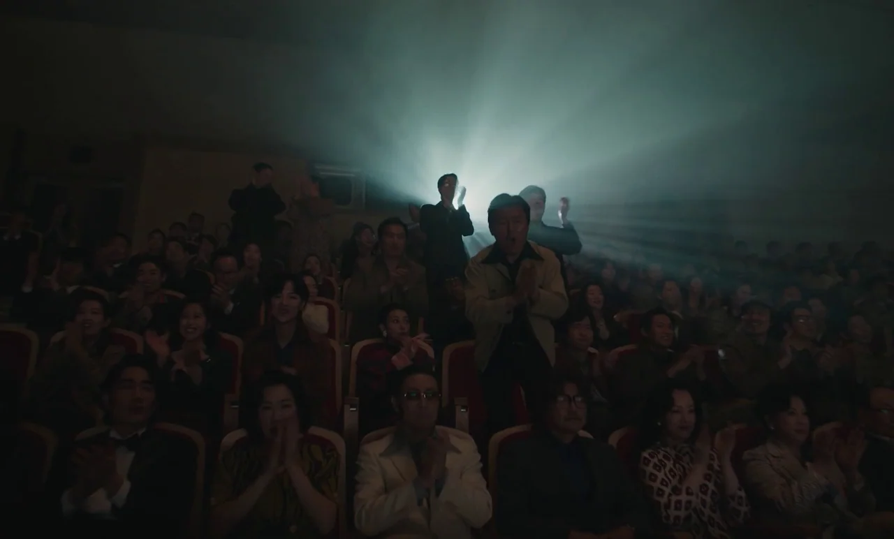 Cobweb (거미집) (2023) movie still: wide — A crowded cinema theater filled with people sitting in rows of red velvet seats. The audience members clap…
