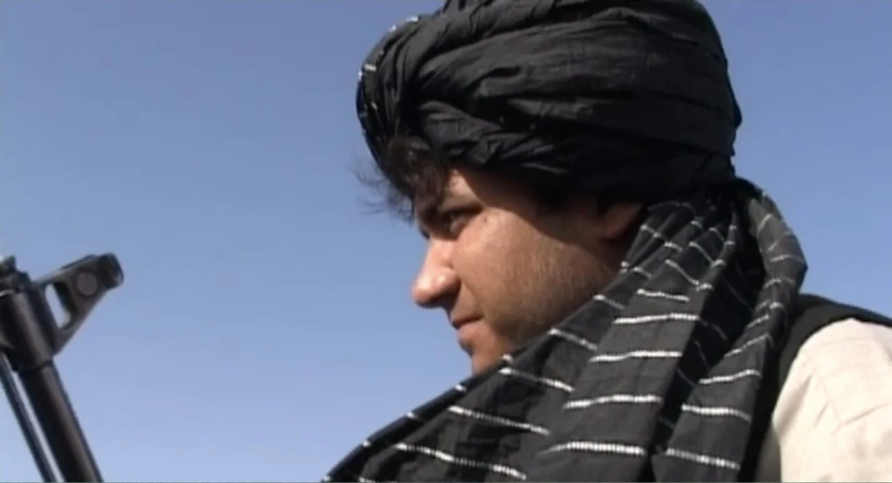 Afghanistan's Opium Trail (2007) movie still: closeup — A man stands outdoors under a clear blue sky in a bright environment. The subject wears a…