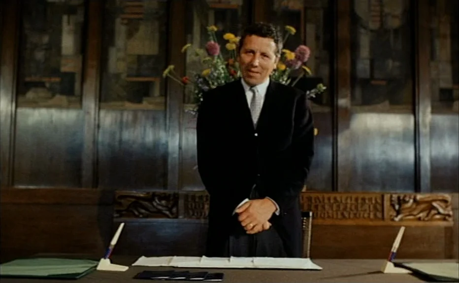 Turkish Delight (1973) movie still: medium — A dark wood-paneled room features elaborate carved carvings along the mid-wall molding. A man in a suit…