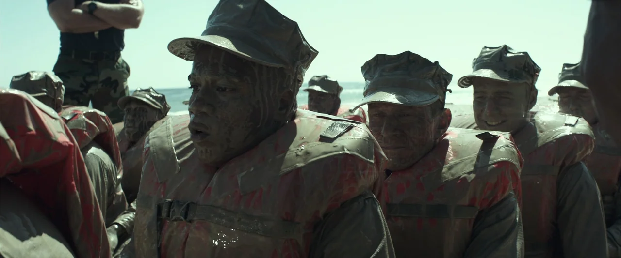 American Sniper (2014) movie still: medium — A group of men in military uniforms and life vests stand on a beach. All subjects have their faces and…