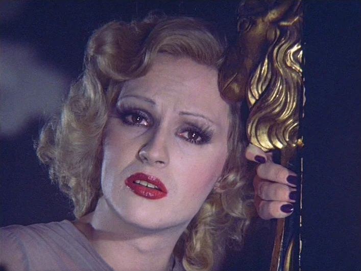 The Death of Maria Malibran (1972) movie still: closeup — A close view of a person with elaborate theatrical makeup and curled blonde hair. The…