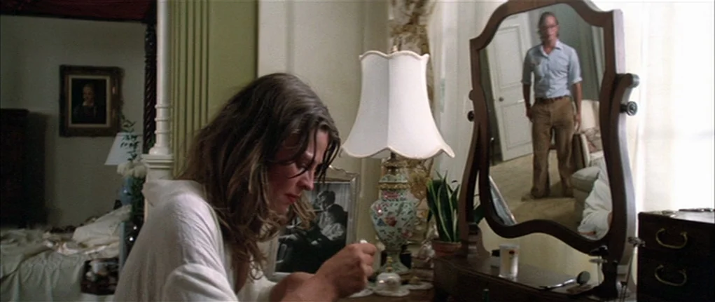 Demon Seed (1977) movie still: medium — A woman sits at a vanity table facing away from the camera in a room. Her male partner stands in the…