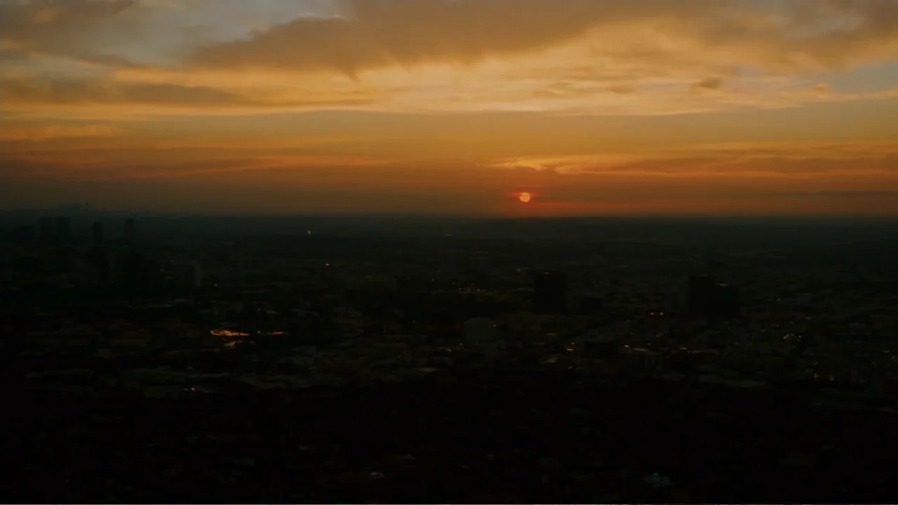Hancock (2008) movie still: establishing — A panoramic aerial view of a city during sunset with scattered buildings below. The sun hangs just above…