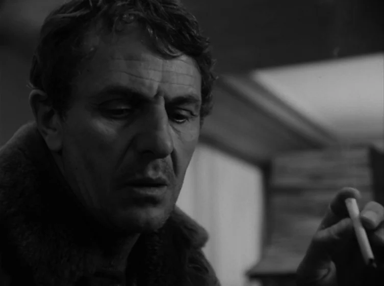 From the Life of the Marionettes (1980) movie still: closeup — An dimly lit interior space with shadows obscuring the surrounding details. A man…
