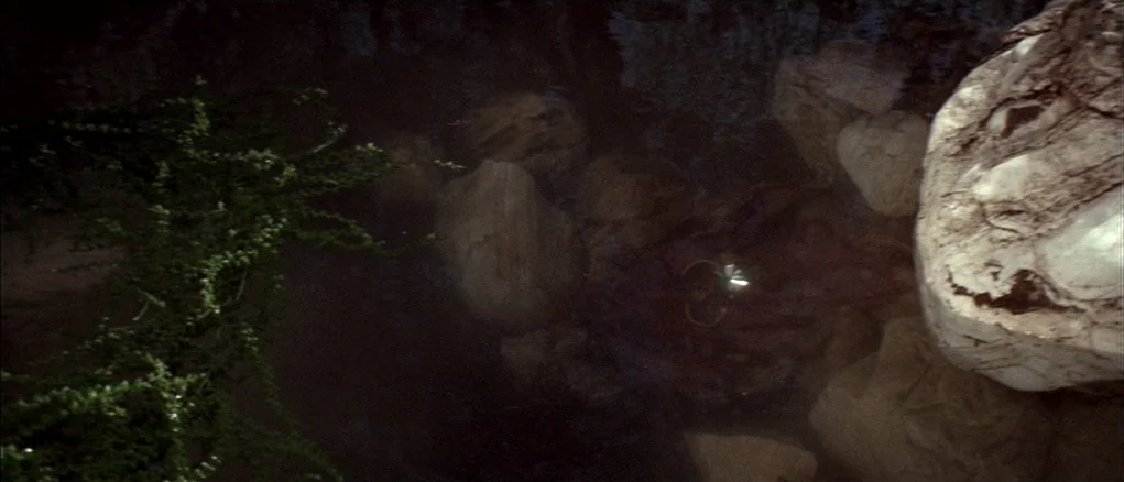 Chinatown (1974) movie still: establishing — A dark rocky stream bed at night is mostly obscured by deep shadows. A small bright object rests among…