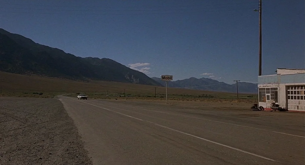 Vanishing Point (1971) movie still: establishing — An asphalt road cuts through a desolate desert valley with distant, arid mountains. A Mobil gas…