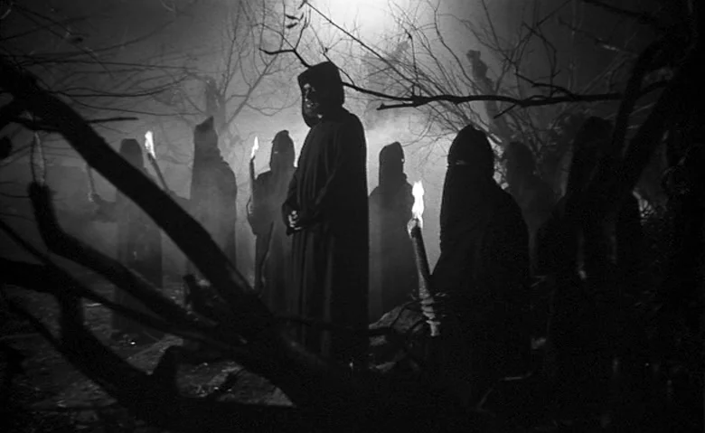 Black Sunday (1960) movie still: medium — A group of cloaked figures in a dark, foggy woodland area at night. Each figure stands among barren,…