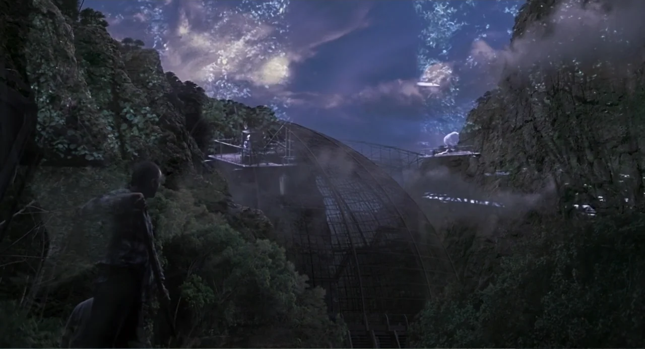 Jurassic Park III (2001) movie still: wide — A dark mountainous gorge holds a large metal structure nestled between steep rocky cliffs. A lone…