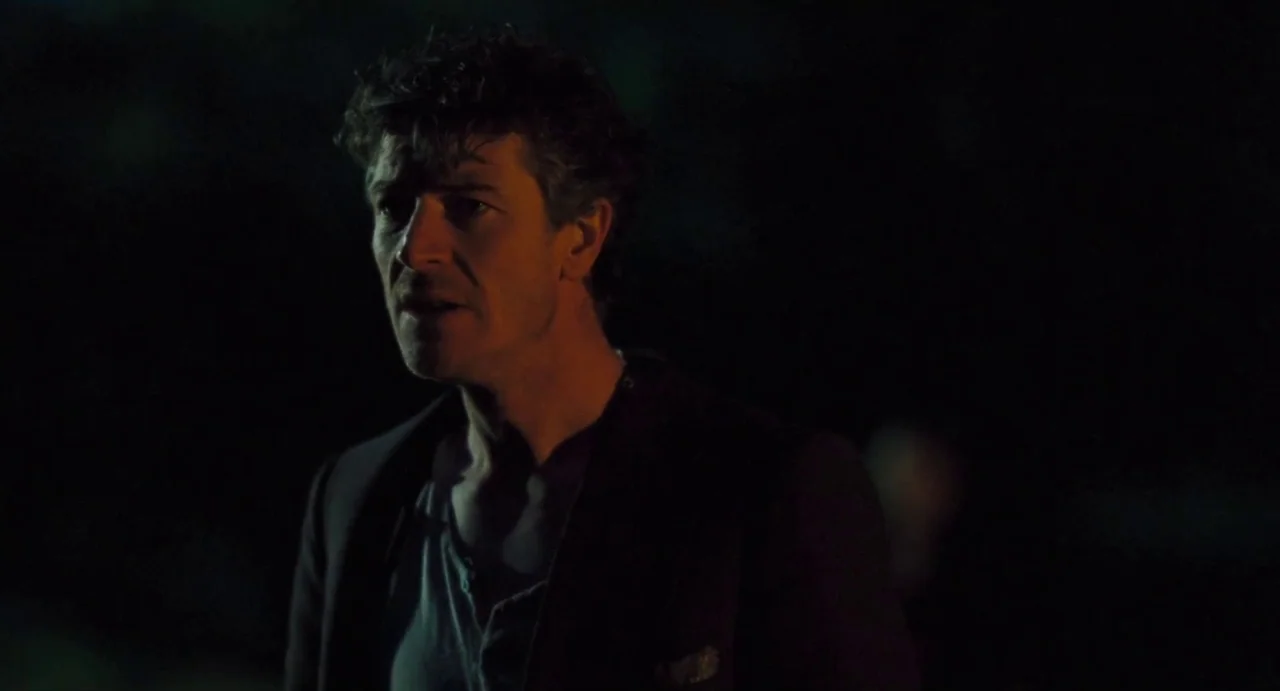 Jimmy’s Hall (2014) movie still: closeup — An outdoor area is completely submerged in darkness during the night. A man stands in profile while…