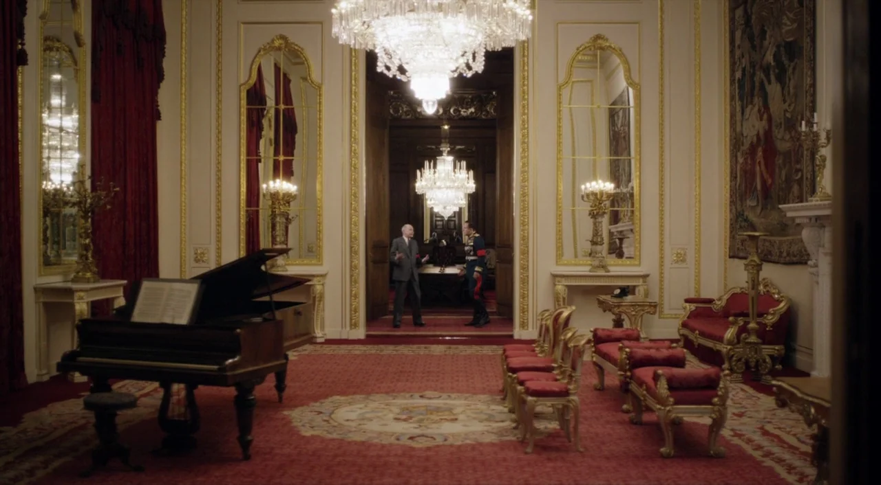 The Death of Stalin (2017) movie still: wide — A grand, opulent room with red carpeting, gold-leaf molding, and large crystal chandeliers. Two men…