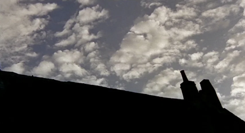 Malpertuis (1971) movie still: establishing — A sharp, dark silhouette of a slanted roof and two chimneys against a sky. White, scattered clouds…