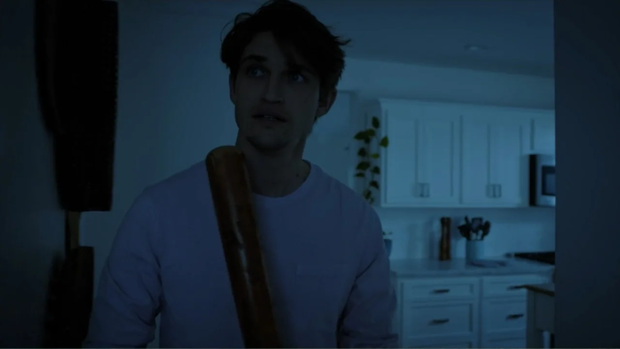 Storm Damage (2000) movie still: medium — A dimly lit room reveals a modern white kitchen in the background. A young man stands in the foreground…
